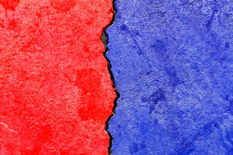 Concrete wall with crack running down the middle painted red on one side and blue on the other